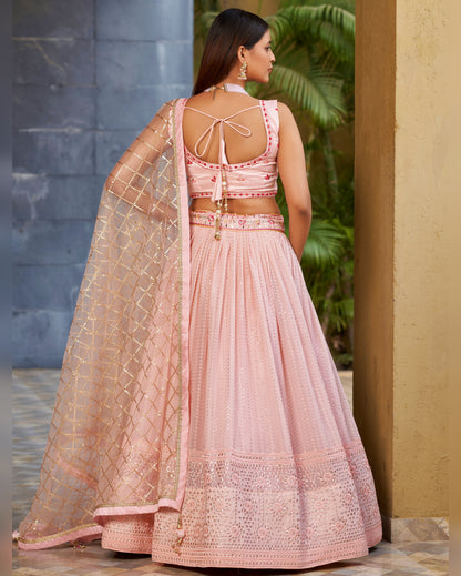 Woman wearing a pink traditional outfit with a textured design, standing in an outdoor setting.