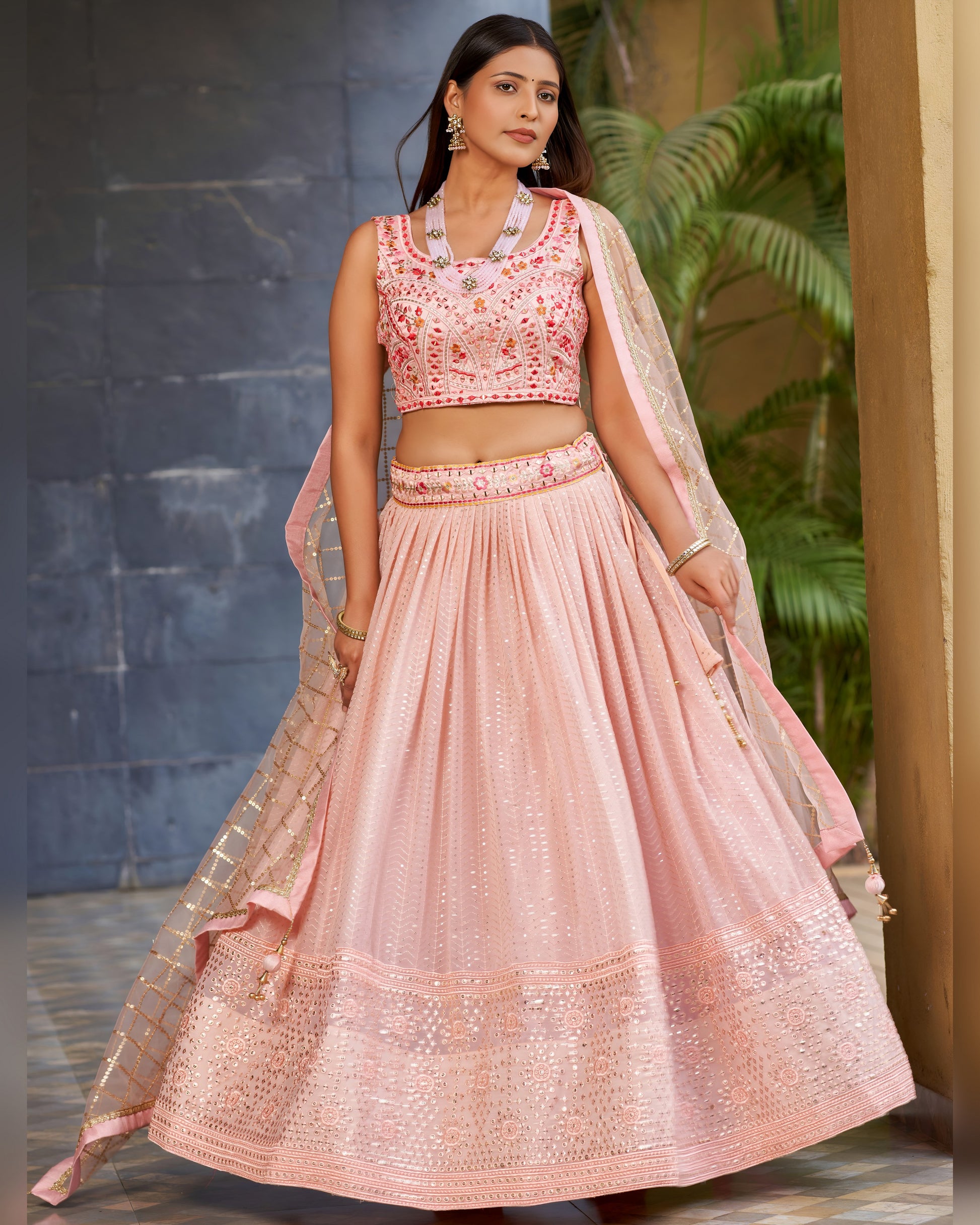Woman wearing a pink embroidered traditional outfit with a dupatta in an outdoor setting.