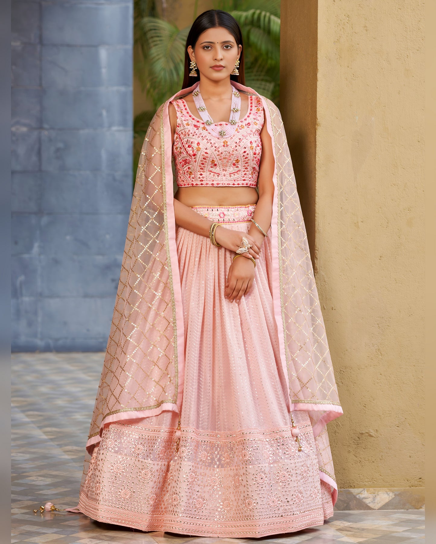 Woman wearing a traditional pink outfit with a dupatta against a neutral background