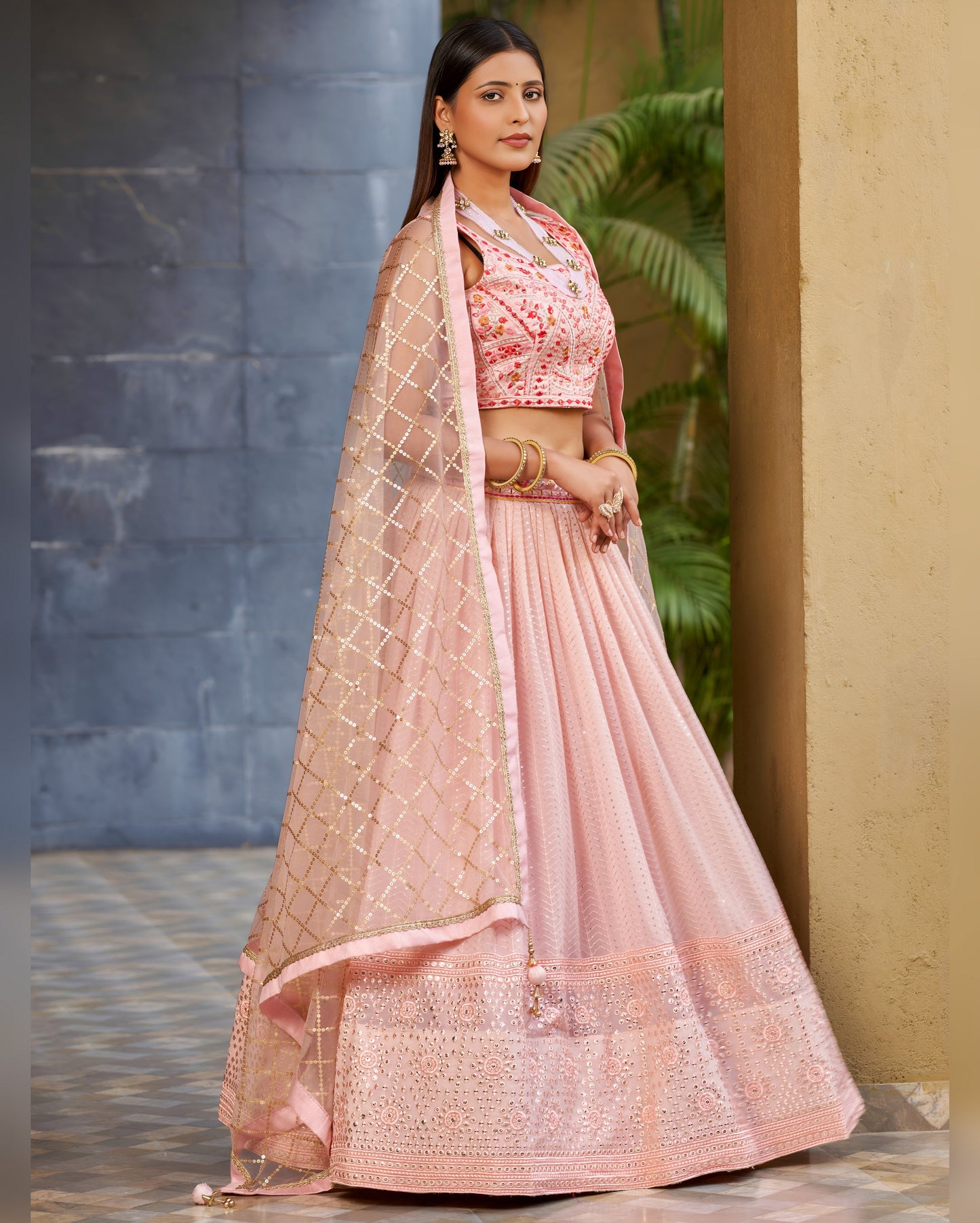 Woman wearing a pink traditional outfit with a floral blouse and net dupatta against a neutral background.