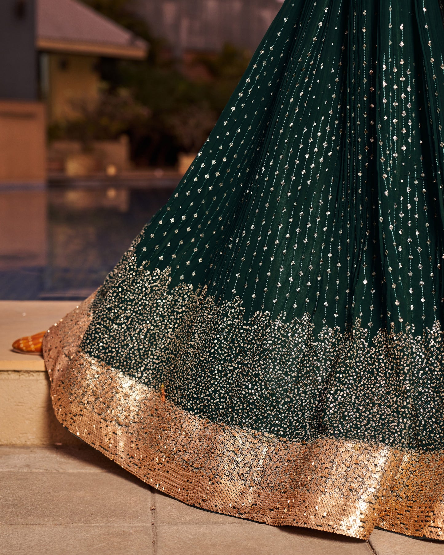 Green and gold traditional outfit with sequin details on a blurred outdoor background