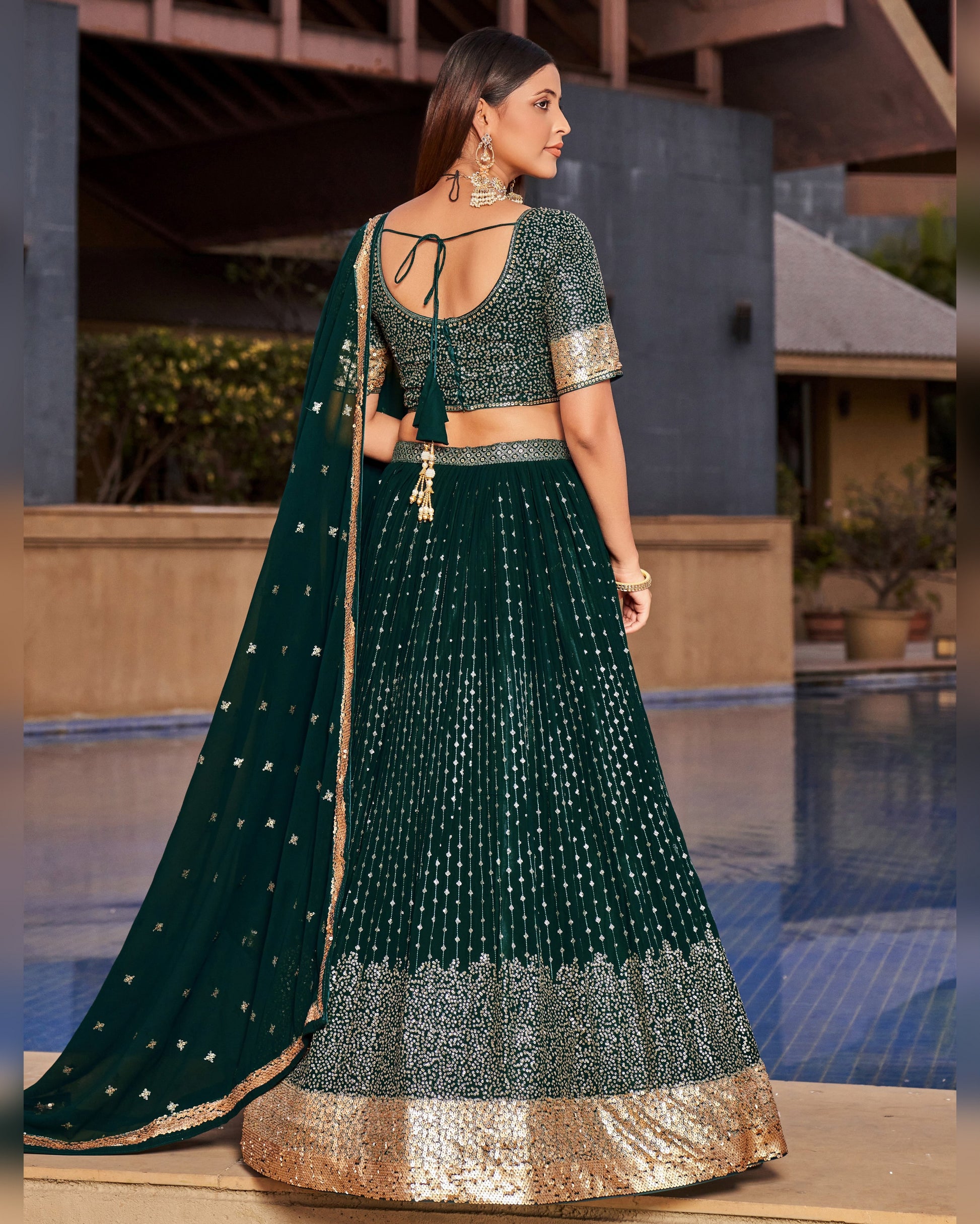 Woman wearing a dark green traditional outfit with gold details by a pool.