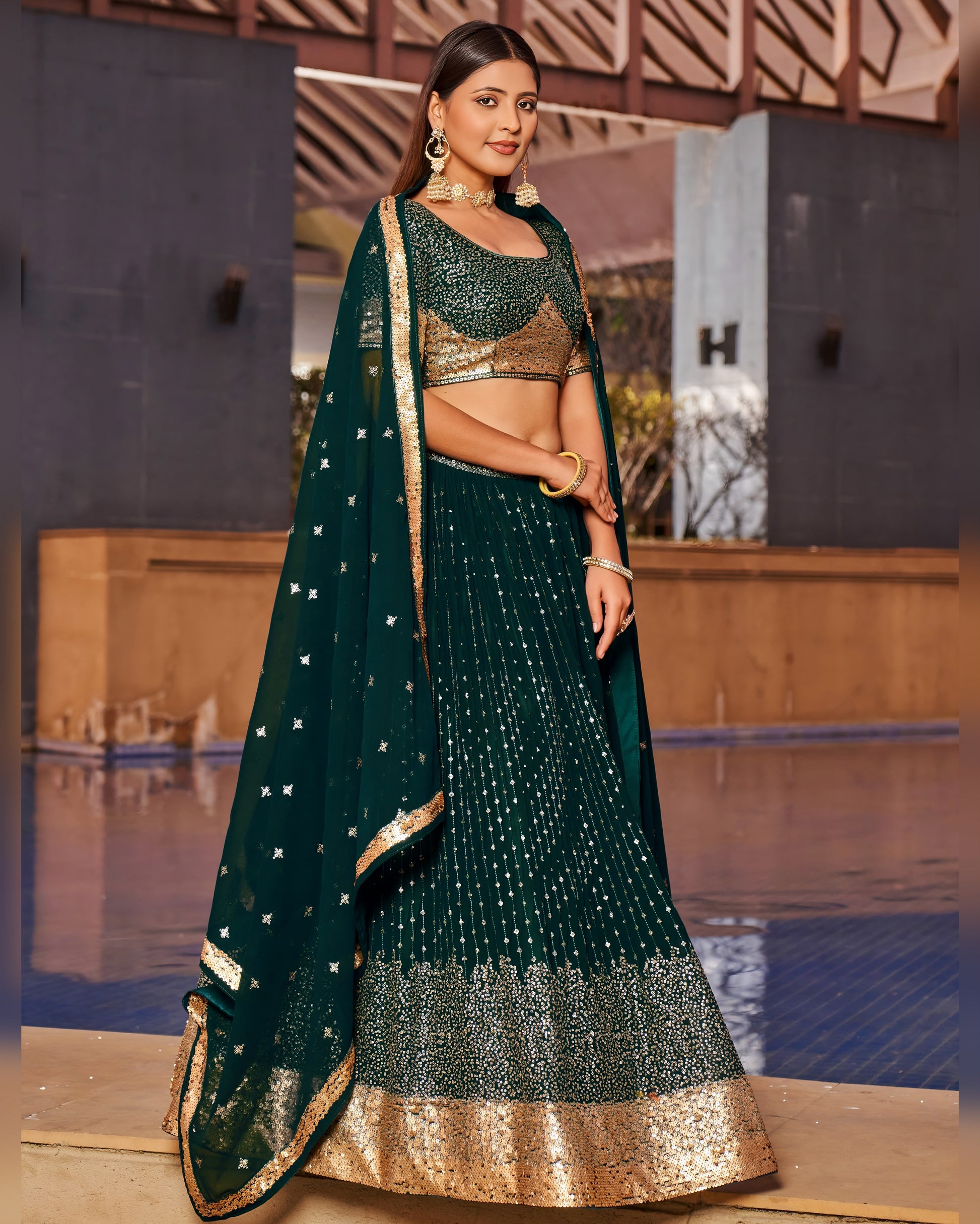 Woman in a green and gold traditional outfit standing by a pool.