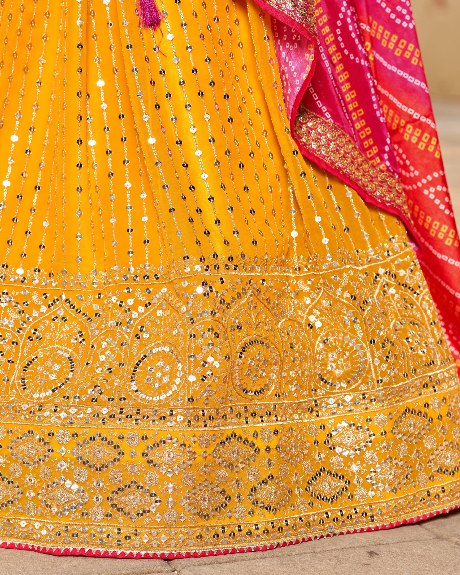 Yellow saree with intricate patterns and a pink border on a wooden surface