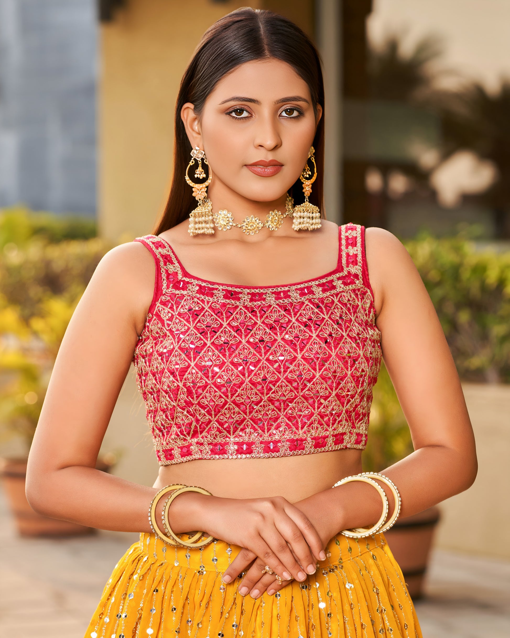 Woman wearing a pink and yellow traditional outfit with jewelry outdoors.