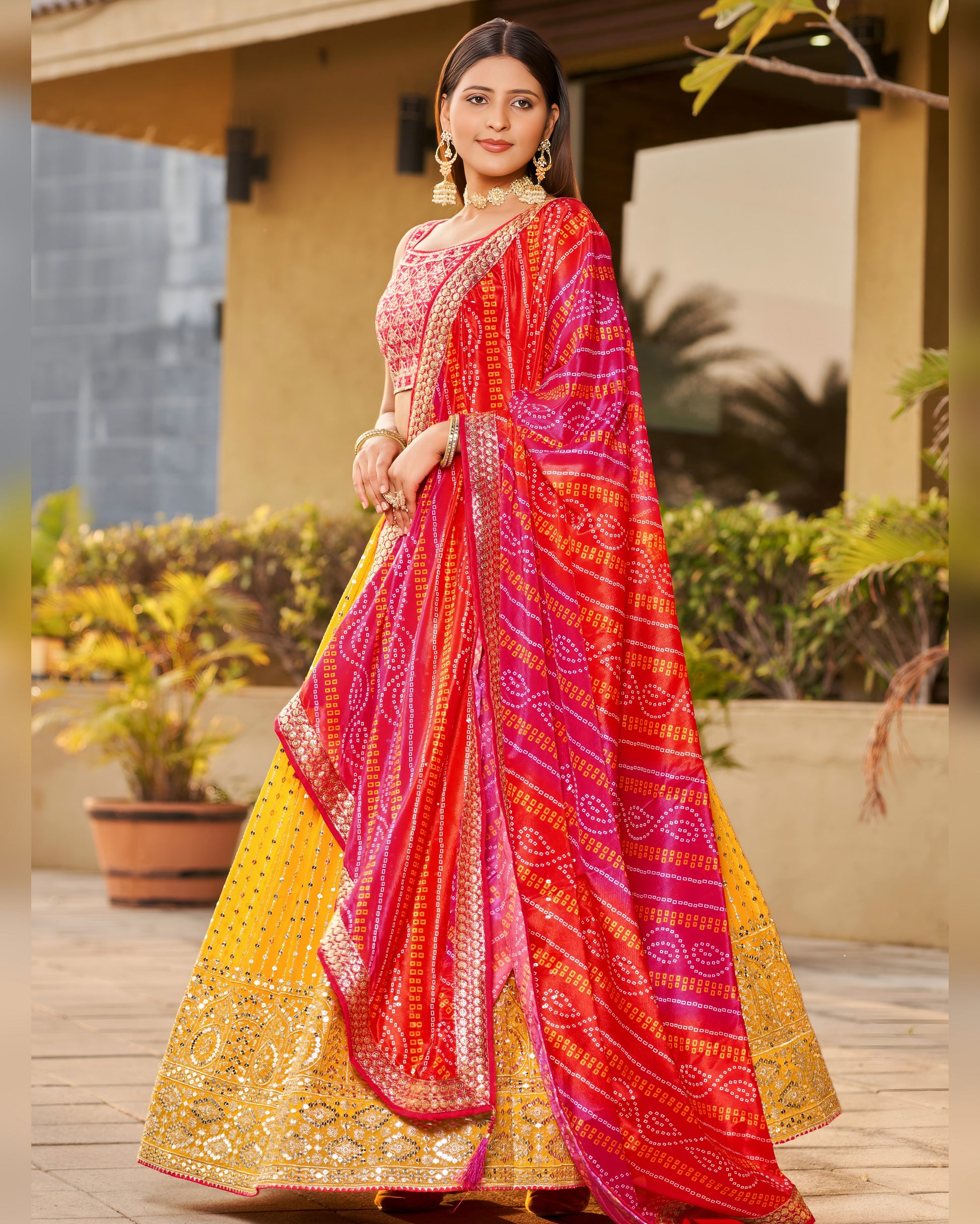 Woman wearing a vibrant red and yellow saree with a patterned border, standing outdoors.