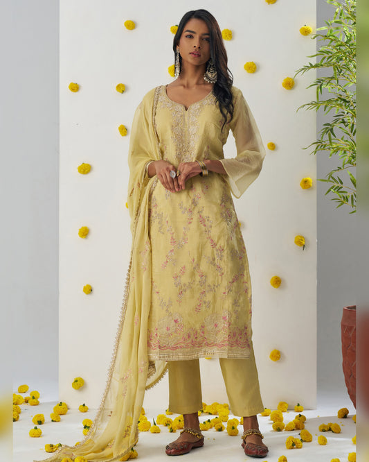 Woman in a light yellow traditional outfit with floral patterns against a decorated wall with yellow flowers.