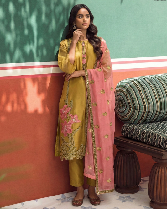 Woman in a yellow and pink traditional outfit standing against a colorful wall.
