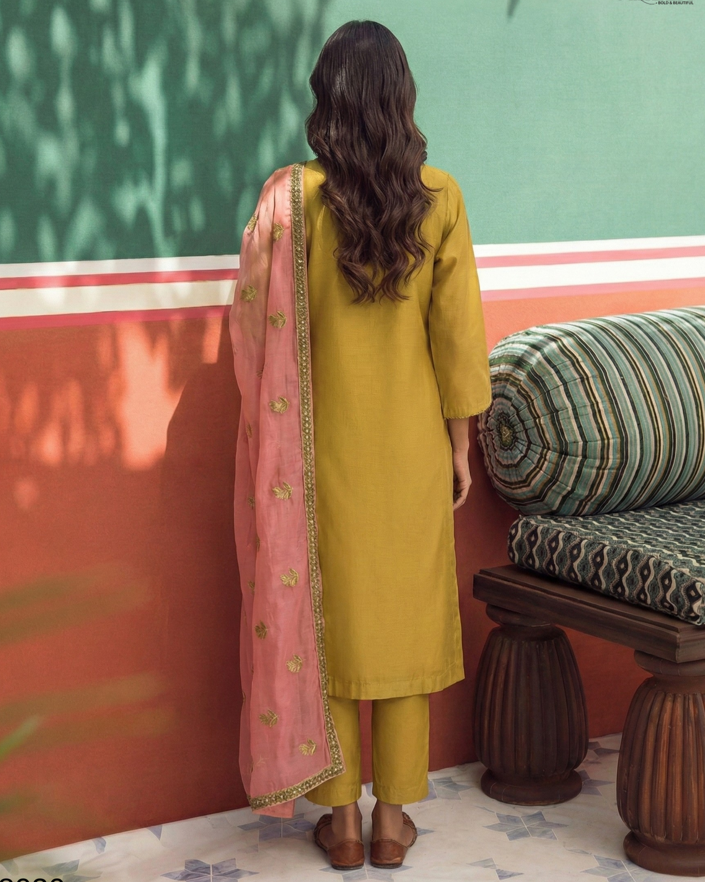 Woman in mustard yellow kurta with pink dupatta standing in front of a colorful wall.