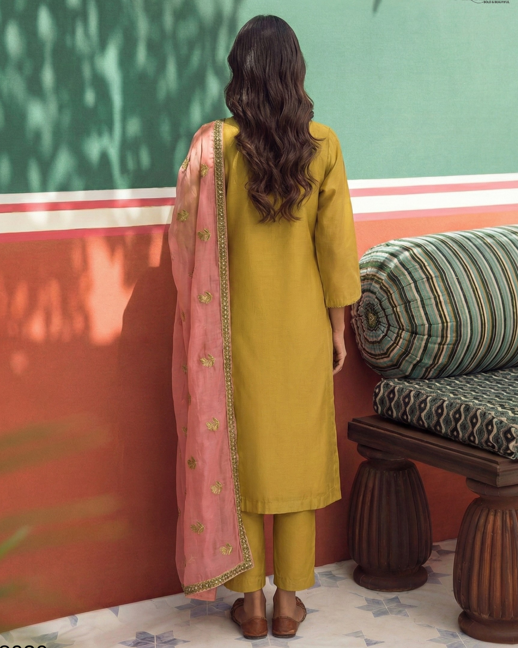 Woman in mustard yellow kurta with pink dupatta standing in front of a colorful wall.