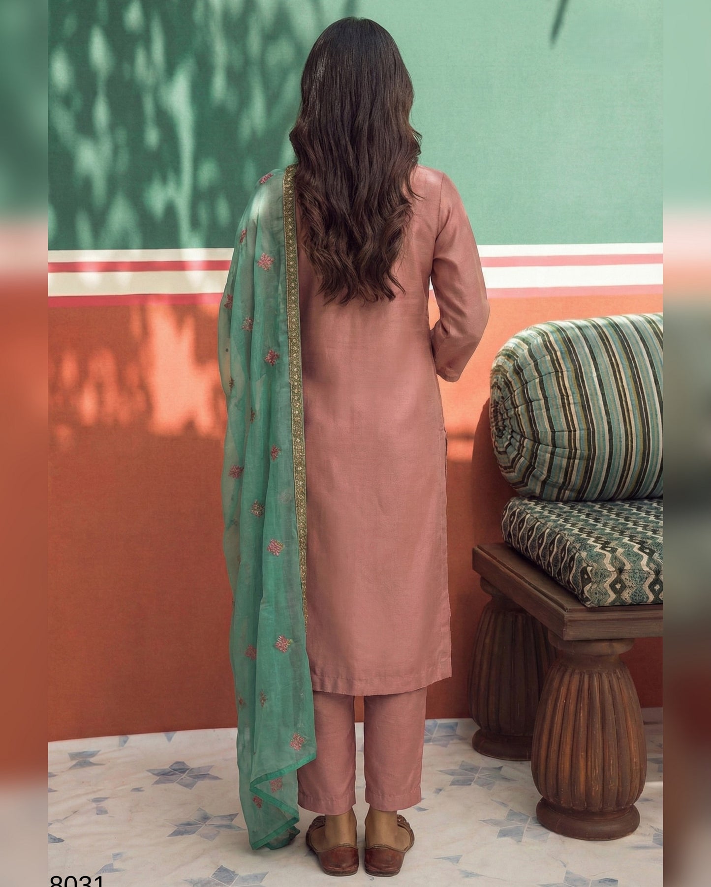 Woman in a pink kurta with a green dupatta standing in a room with a green wall and wooden bench.
