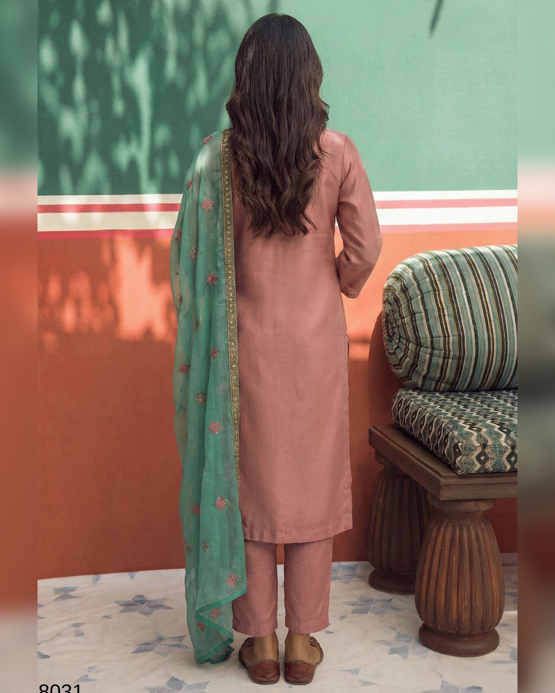 Woman in a pink kurta with a green dupatta standing in a room with a green wall and wooden bench.