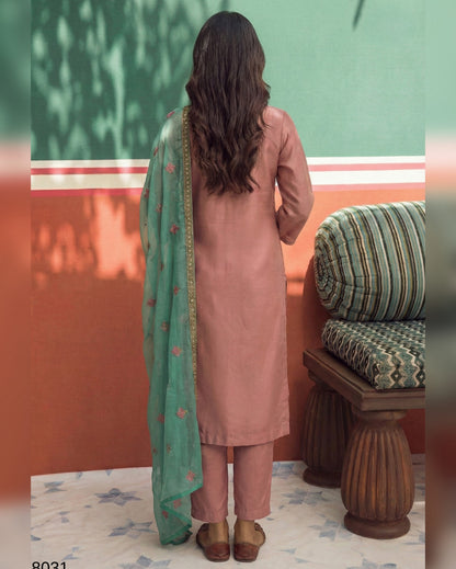 Woman in a pink kurta with a green dupatta standing in a room with a green wall and wooden bench.