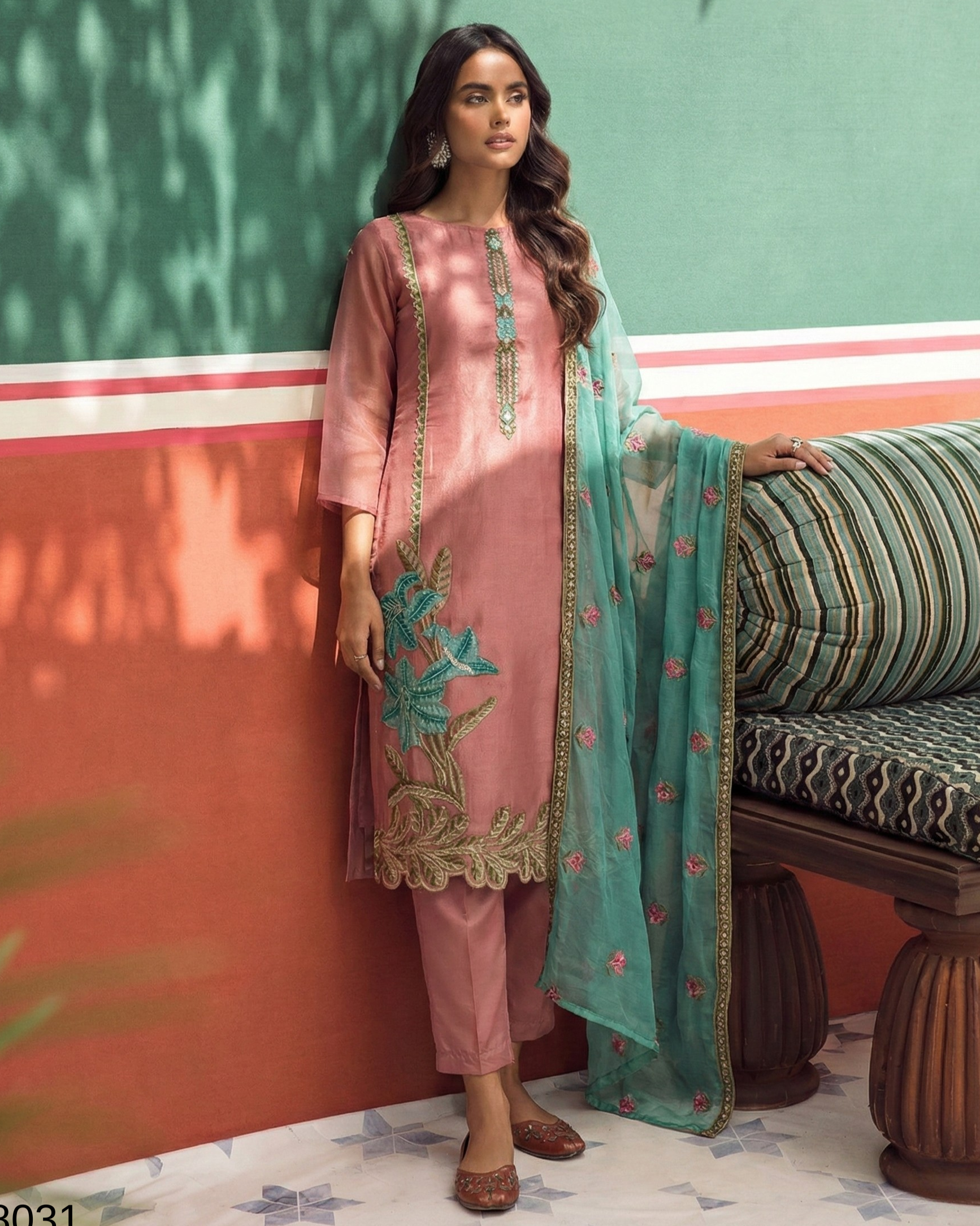 Woman in a pink traditional outfit with teal dupatta against a colorful wall.