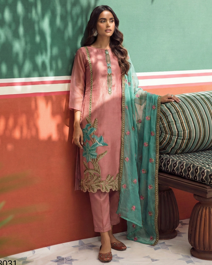 Woman in a pink traditional outfit with teal dupatta against a colorful wall.