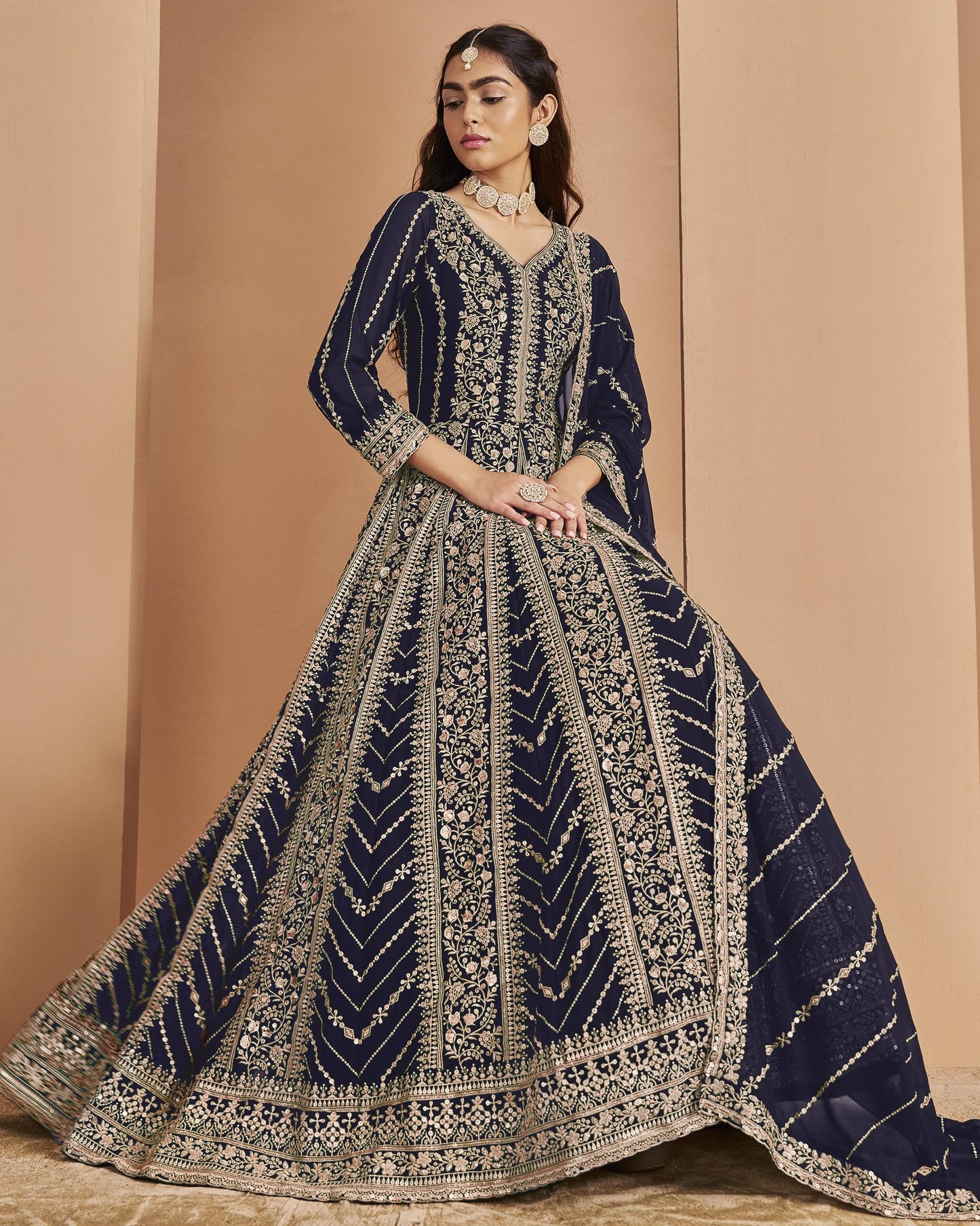 Woman wearing a navy blue and gold embroidered traditional outfit against a beige background