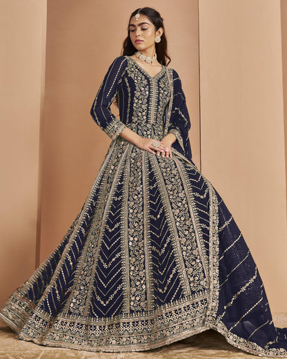 Woman wearing a navy blue and gold embroidered traditional outfit against a beige background