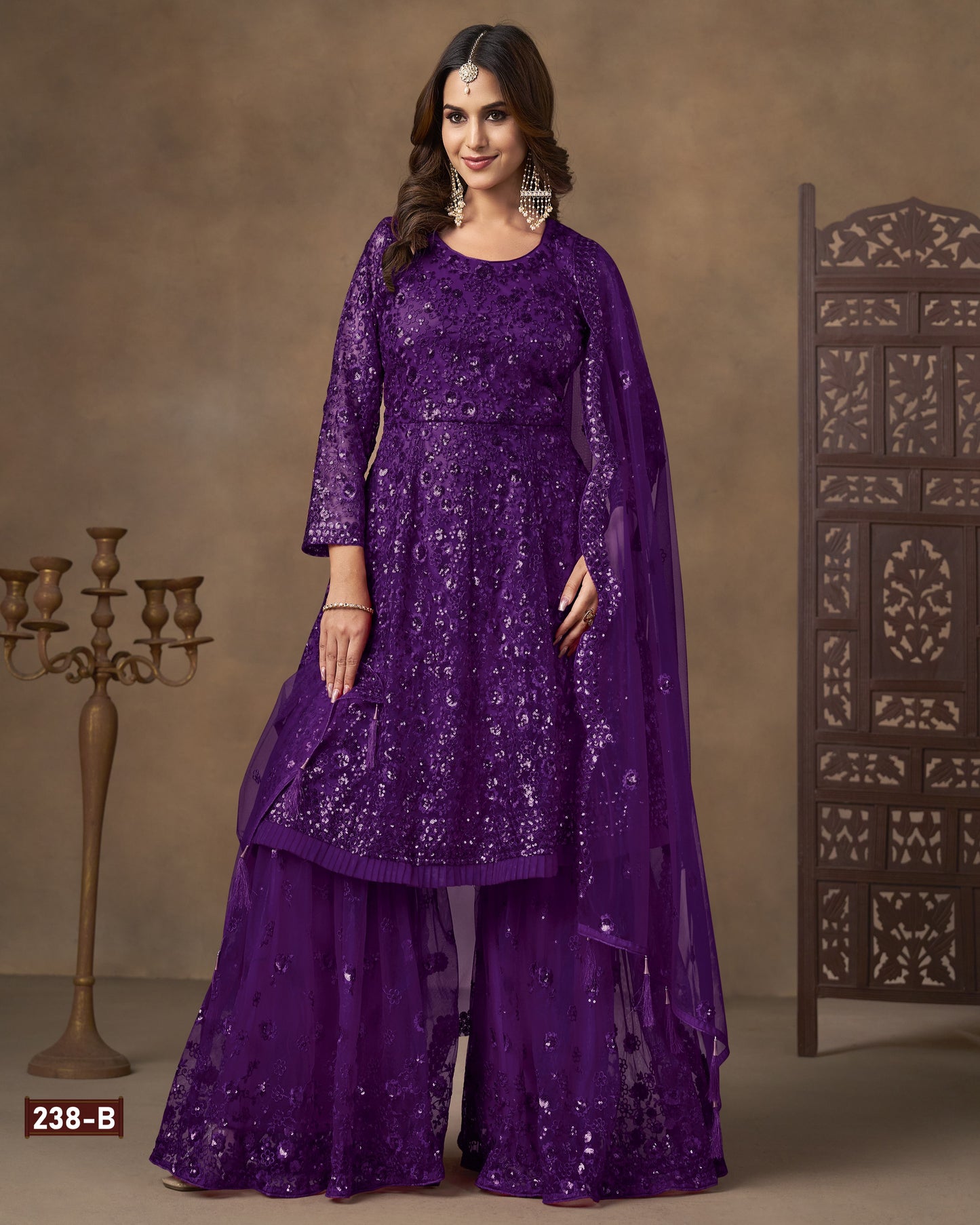Woman wearing a purple embroidered outfit with a matching dupatta against a brown background.
