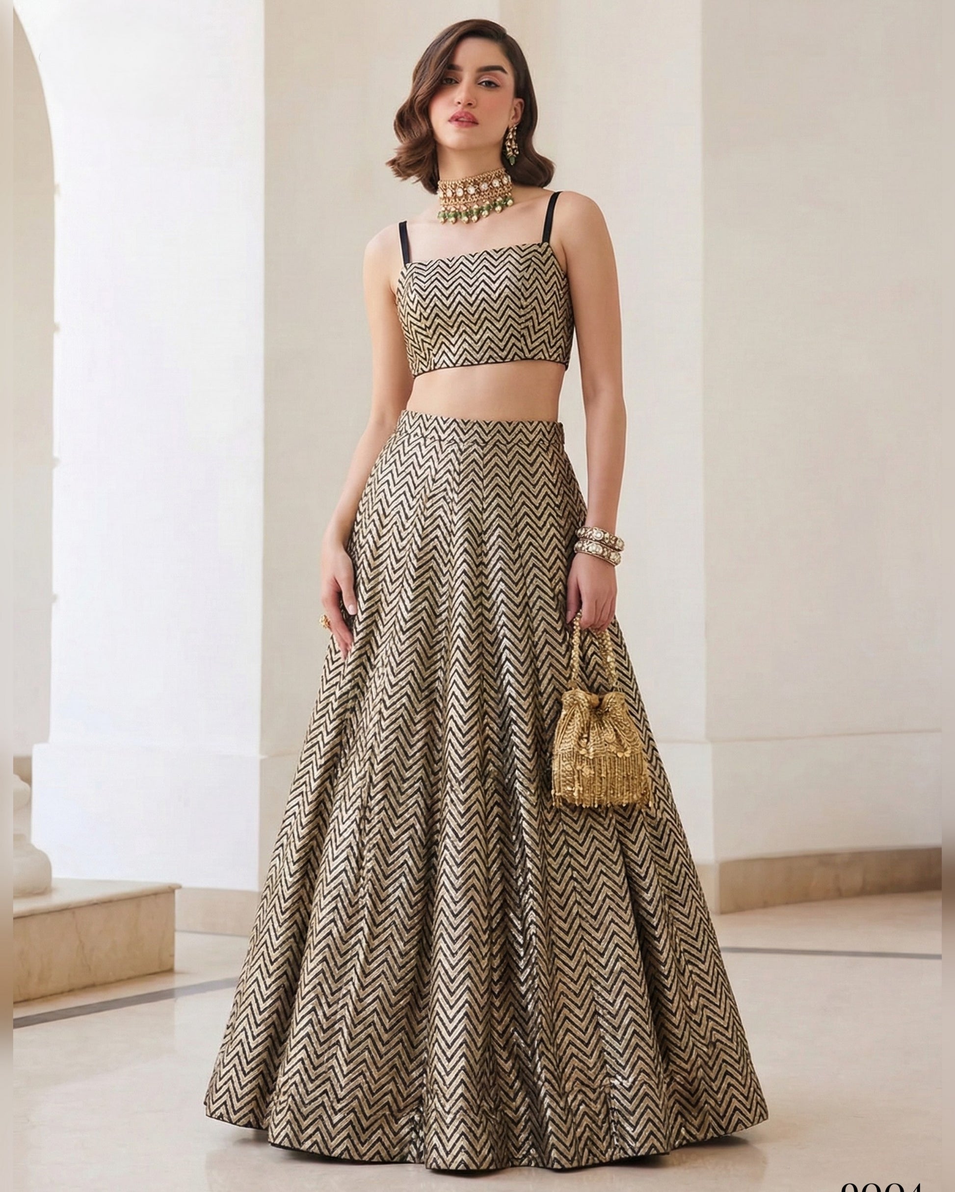 Woman wearing a patterned outfit with a long skirt and top, holding a gold handbag indoors.