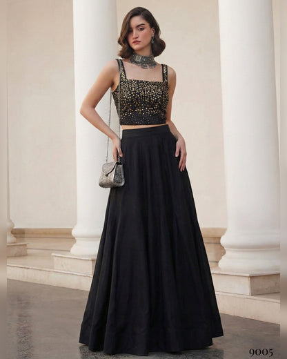 Woman in a black outfit with a studded top standing in an elegant interior setting.