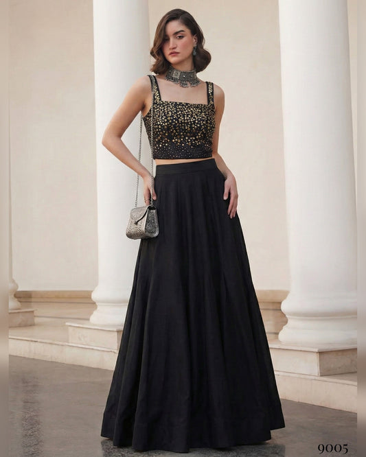 Woman in a black outfit with a studded top standing in an elegant interior setting.