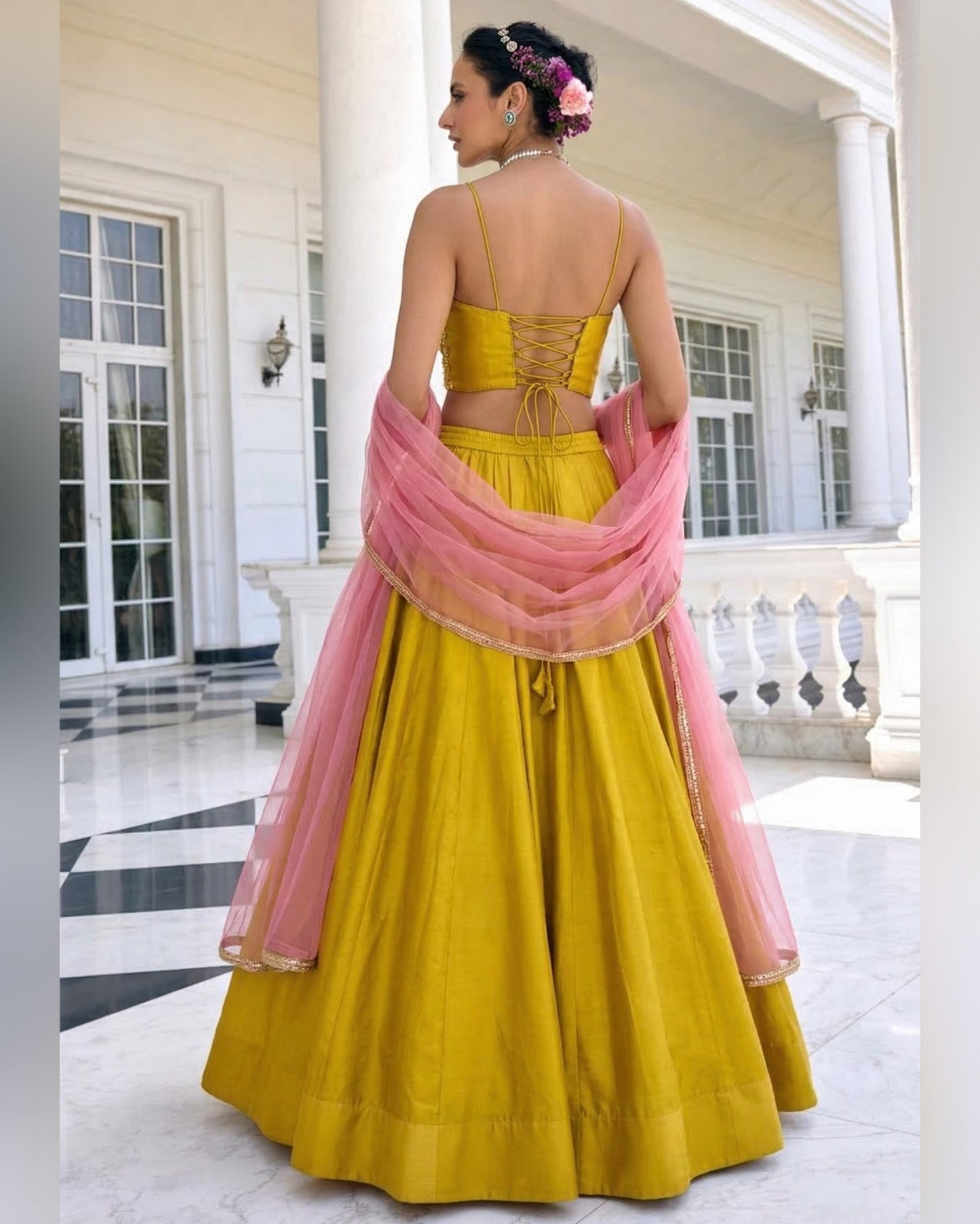 Woman in a yellow and pink traditional outfit standing in a white architectural setting.