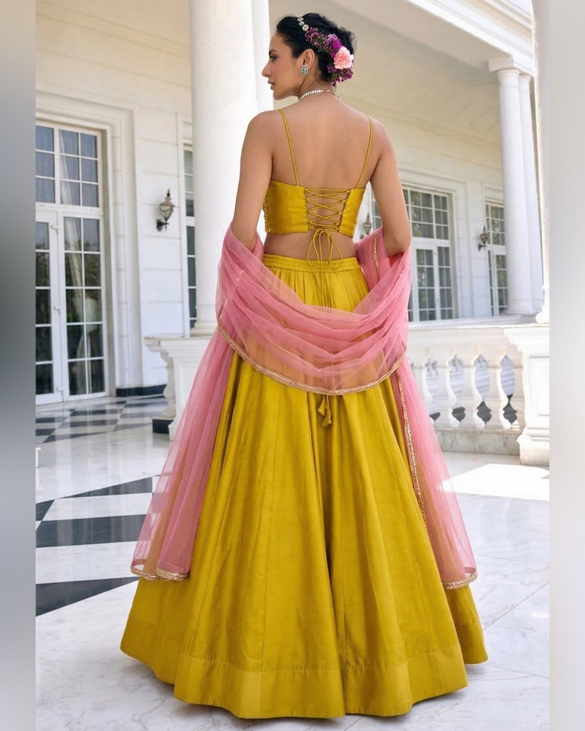 Woman in a yellow and pink traditional outfit standing in a white architectural setting.