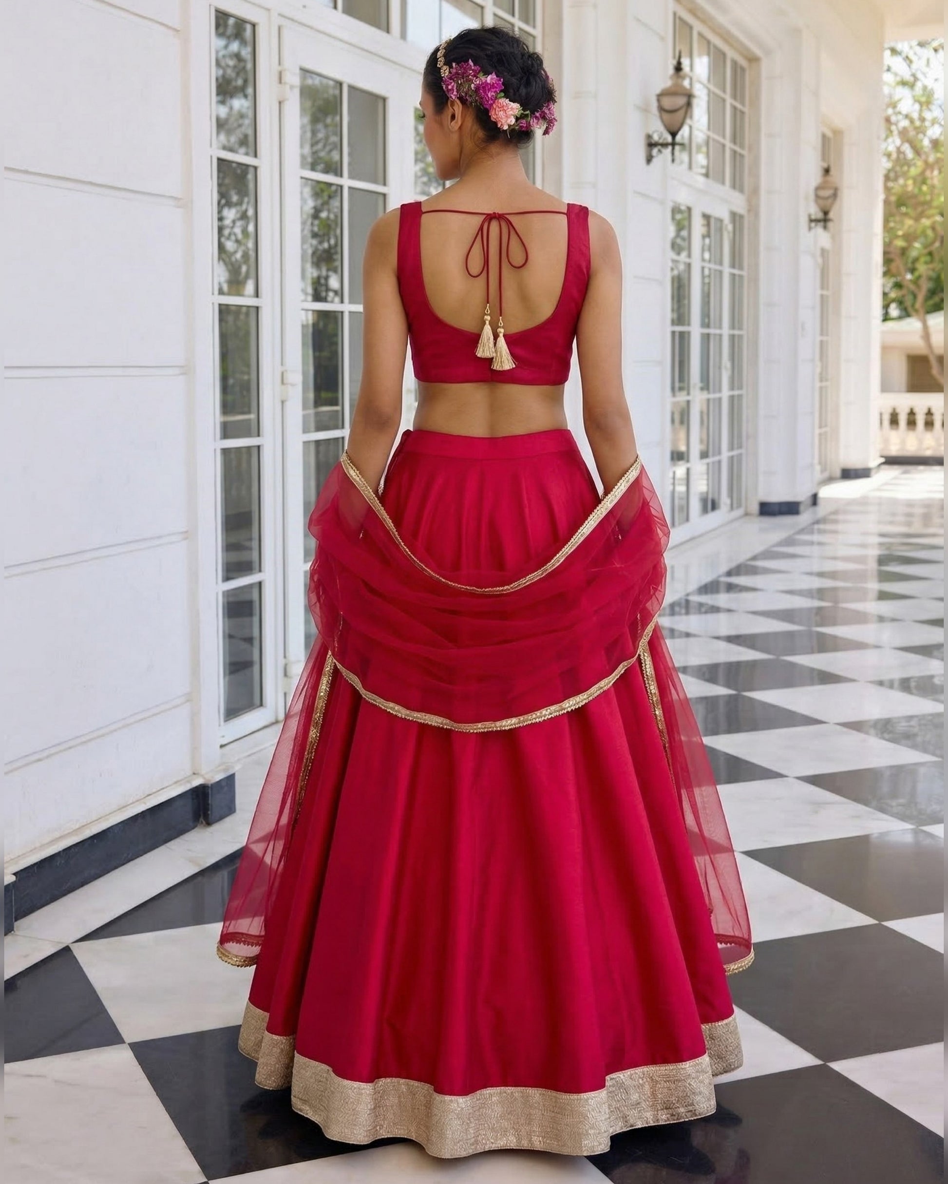 Person wearing a red traditional outfit with gold details in front of a white building.