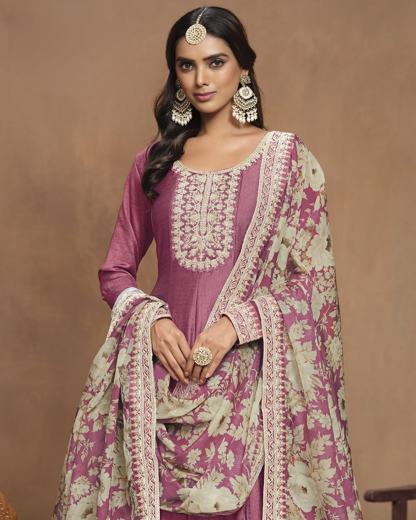 Woman wearing a traditional pink and white embroidered outfit with a brown background