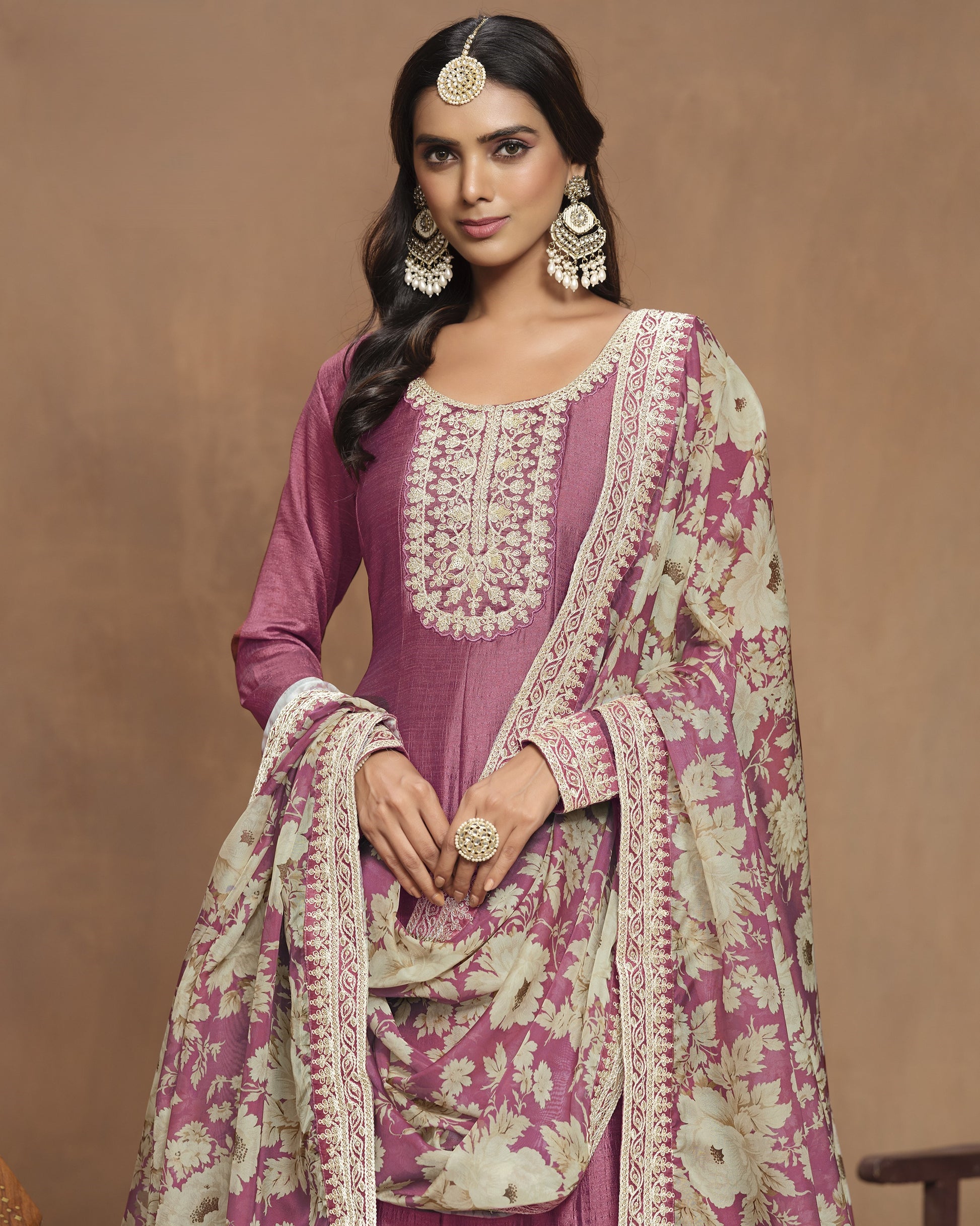 Woman wearing a traditional pink and white embroidered outfit with a brown background