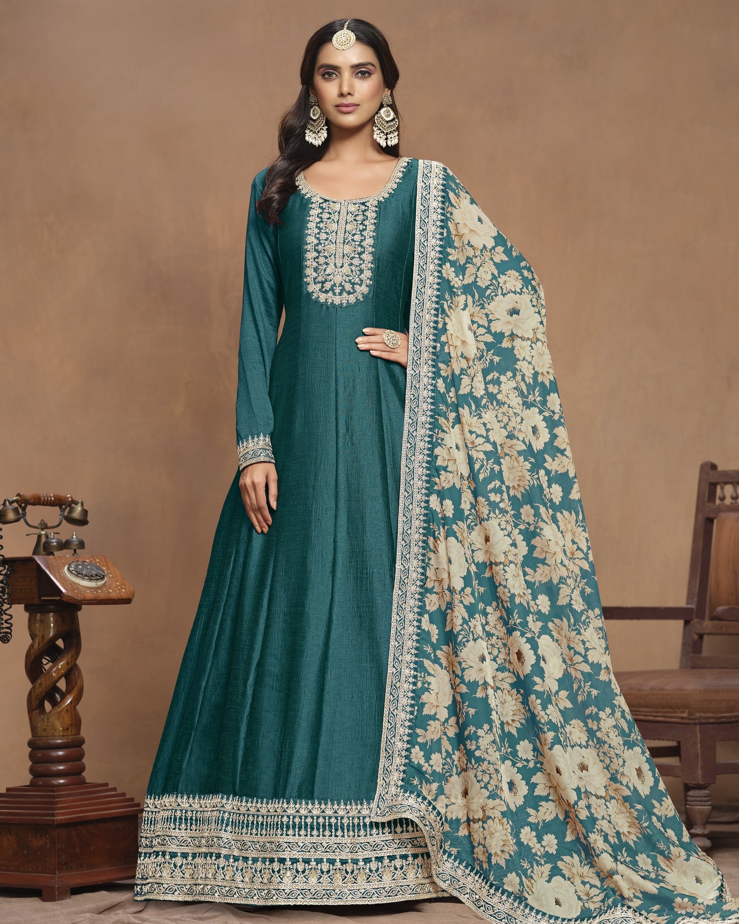 Woman wearing a teal traditional outfit with a floral shawl against a brown background