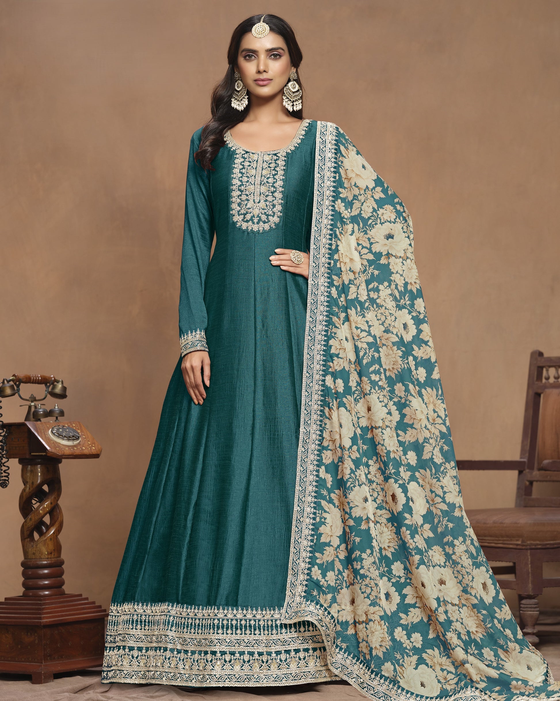 Woman wearing a teal traditional outfit with a floral shawl against a brown background