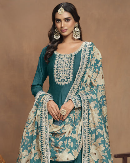 Woman wearing a traditional teal and beige embroidered outfit with jewelry against a brown background