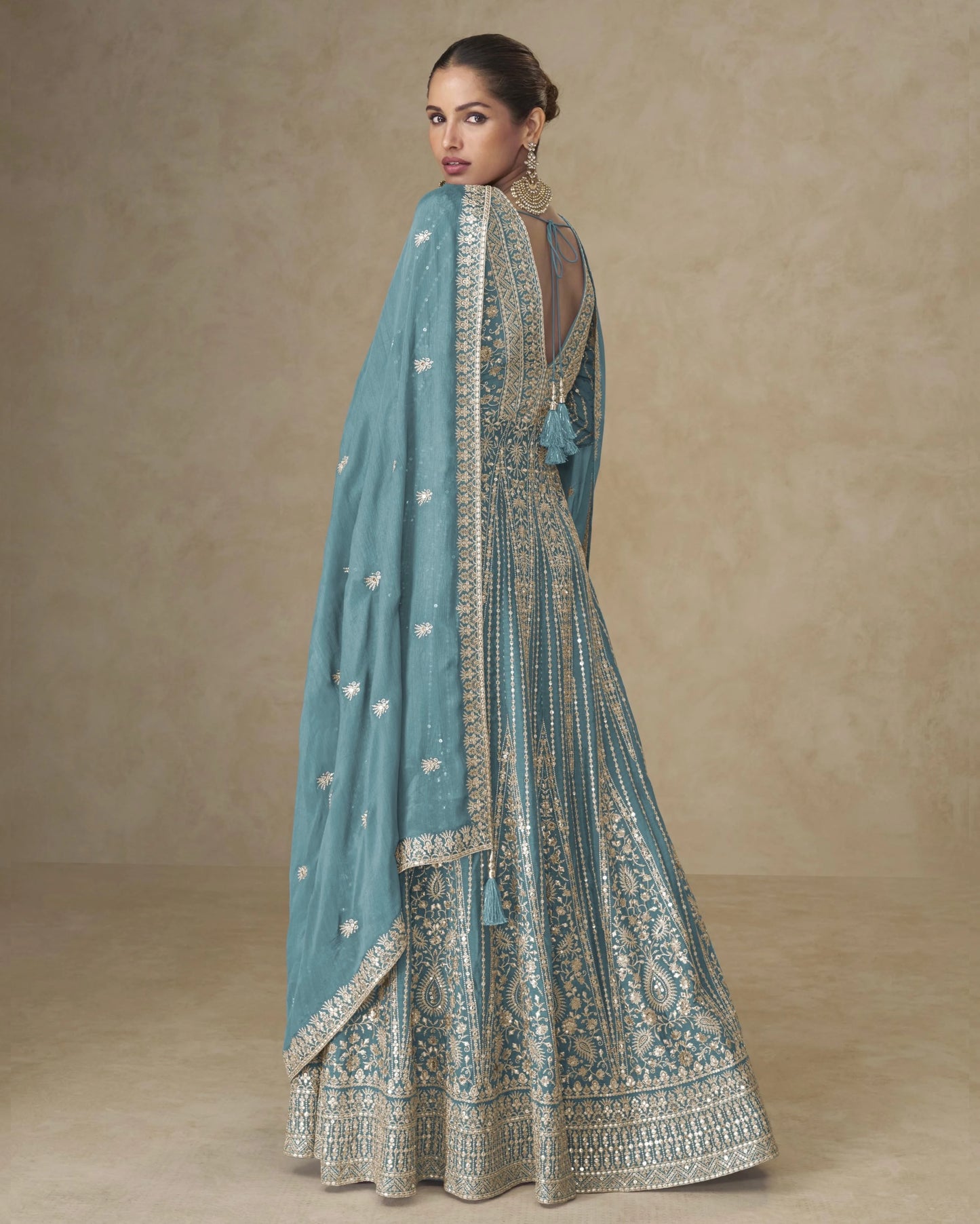 Woman wearing a light blue embroidered traditional outfit with a matching dupatta on a beige background