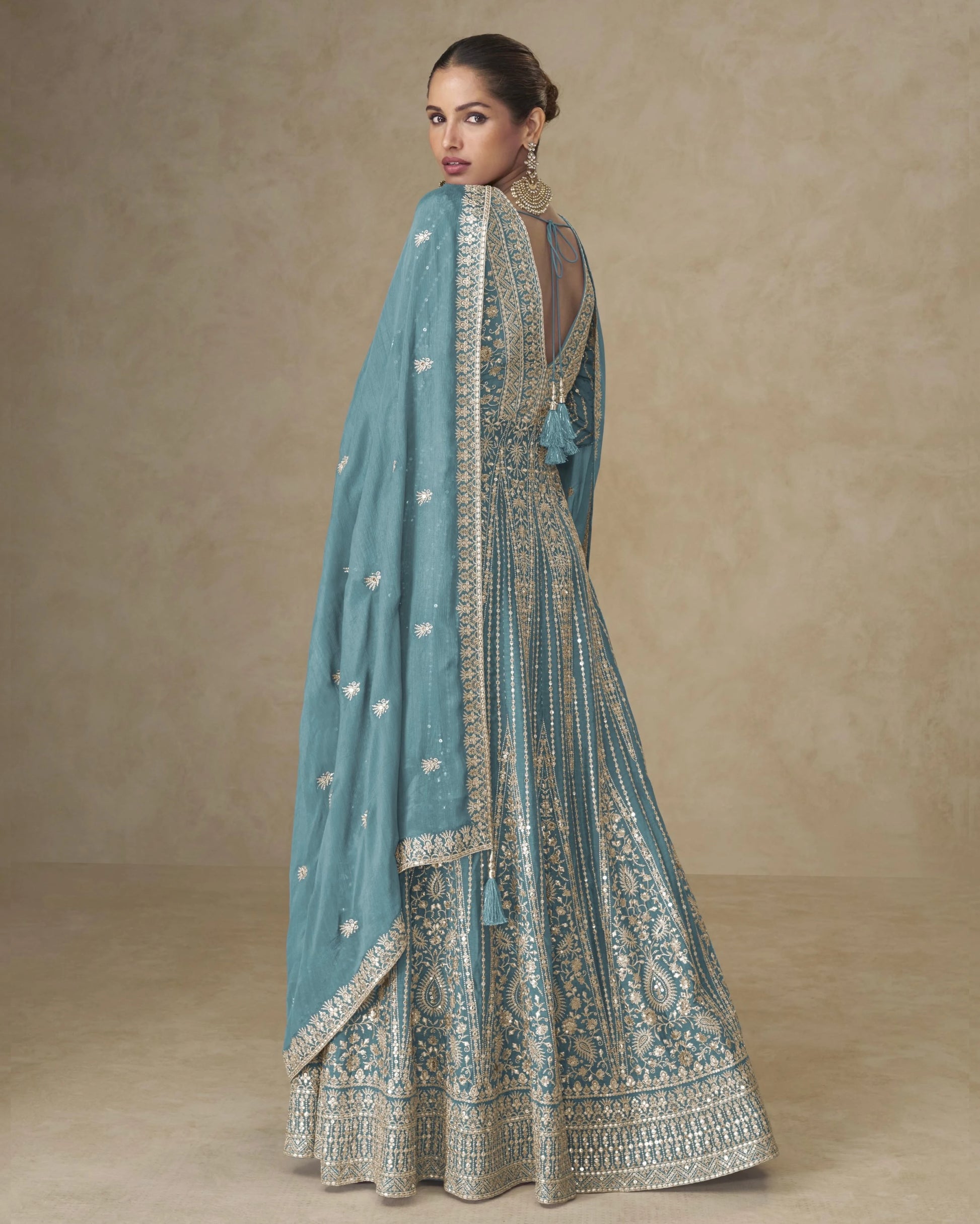 Woman wearing a light blue embroidered traditional outfit with a matching dupatta on a beige background