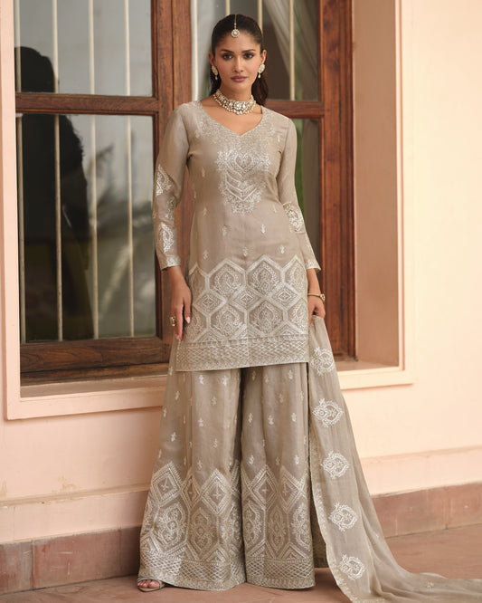 Woman wearing a traditional embroidered outfit in front of a window.