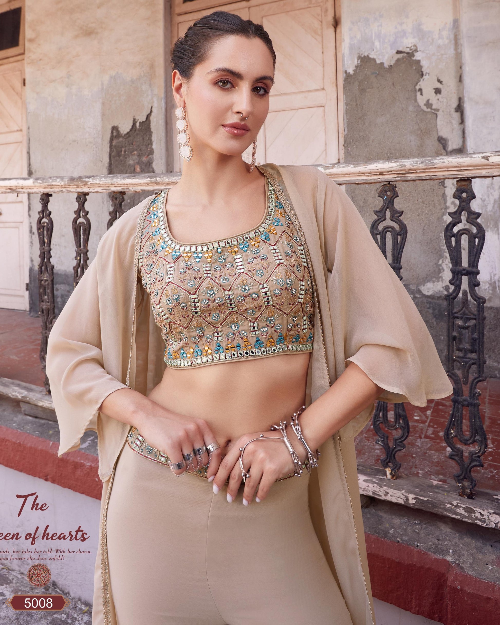 Woman in traditional outfit with intricate design, standing in front of a decorative wall.