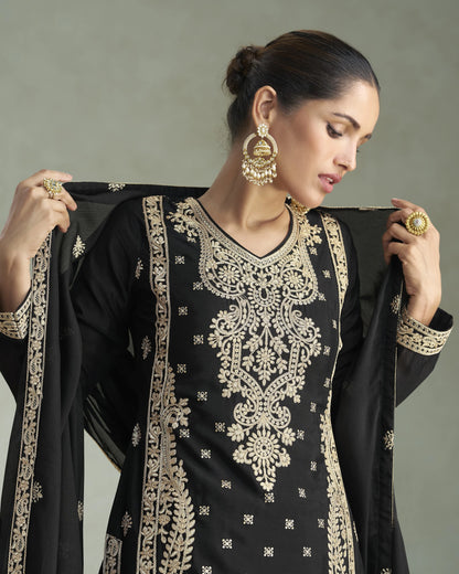 Woman wearing a black and gold embroidered traditional outfit with jewelry.
