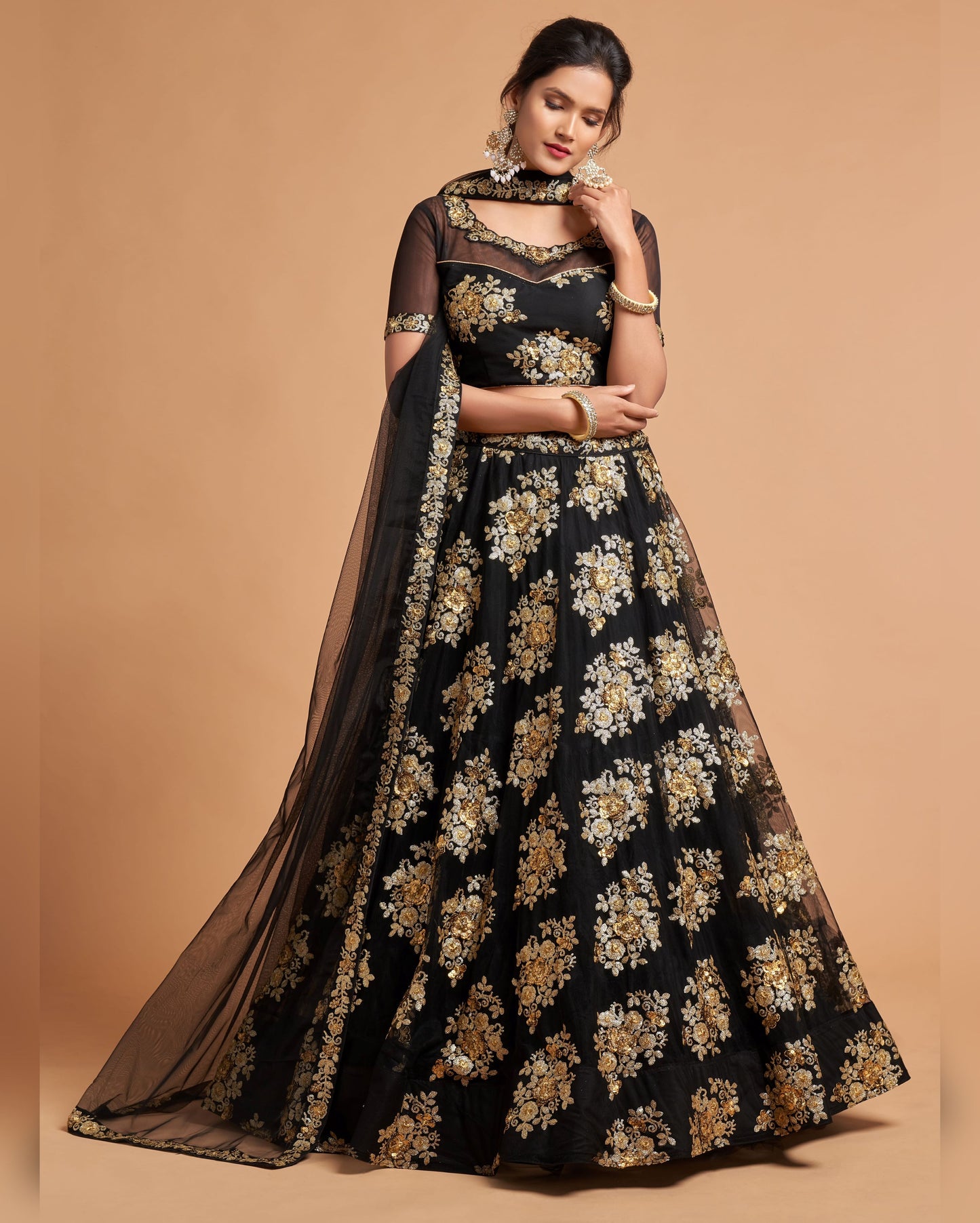 Woman wearing a black and gold floral dress with a sheer dupatta on a beige background