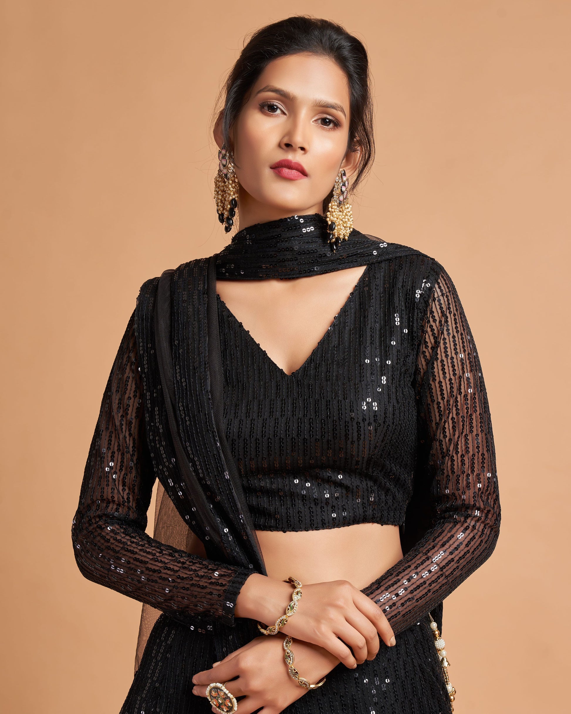 Woman wearing a black sequin outfit with sheer sleeves on a beige background