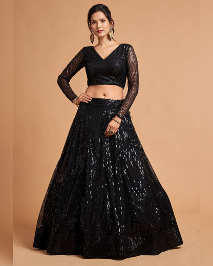 Woman wearing a black embroidered lehenga with sheer sleeves on a beige background