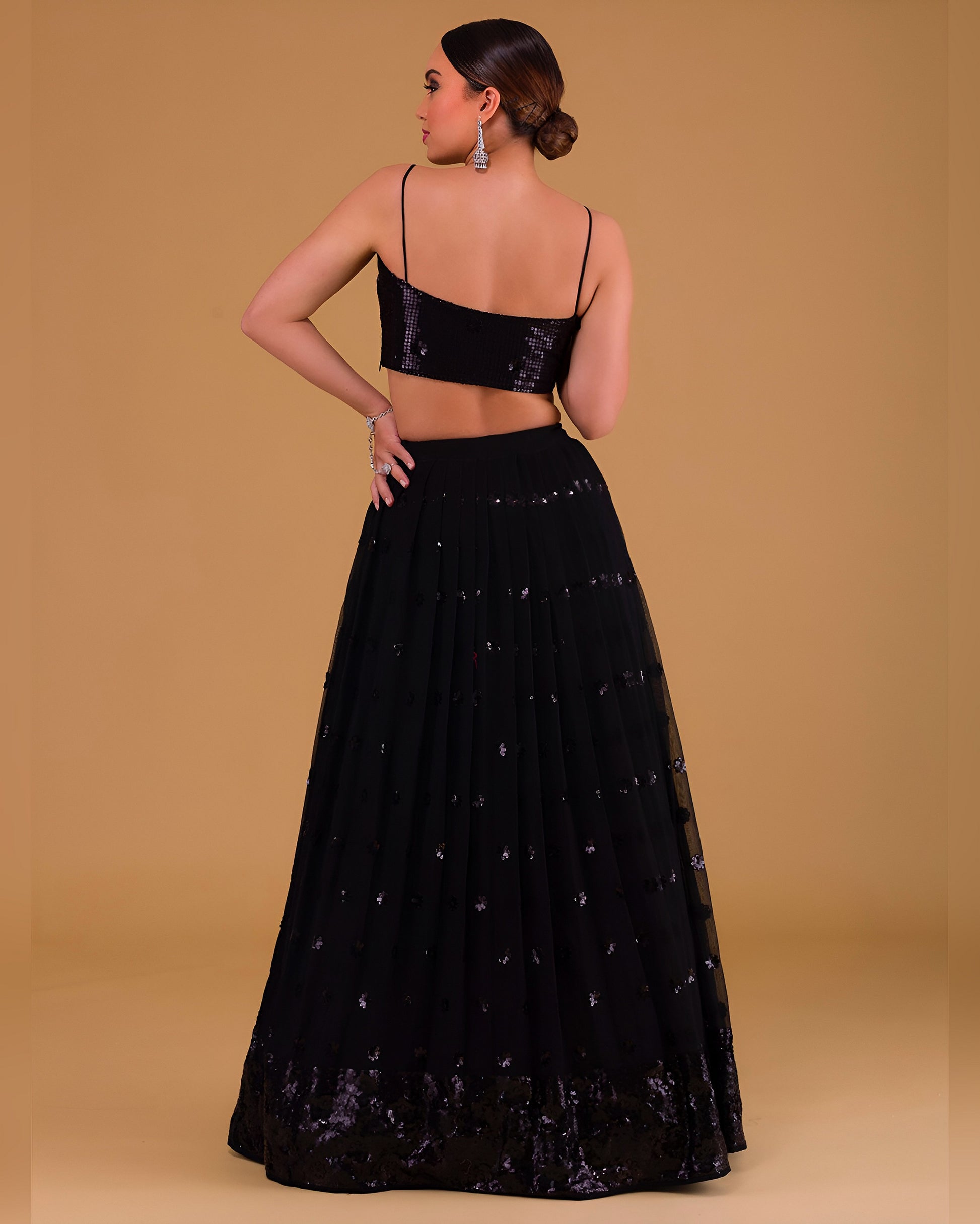 Woman wearing a black embroidered lehenga with a plain background