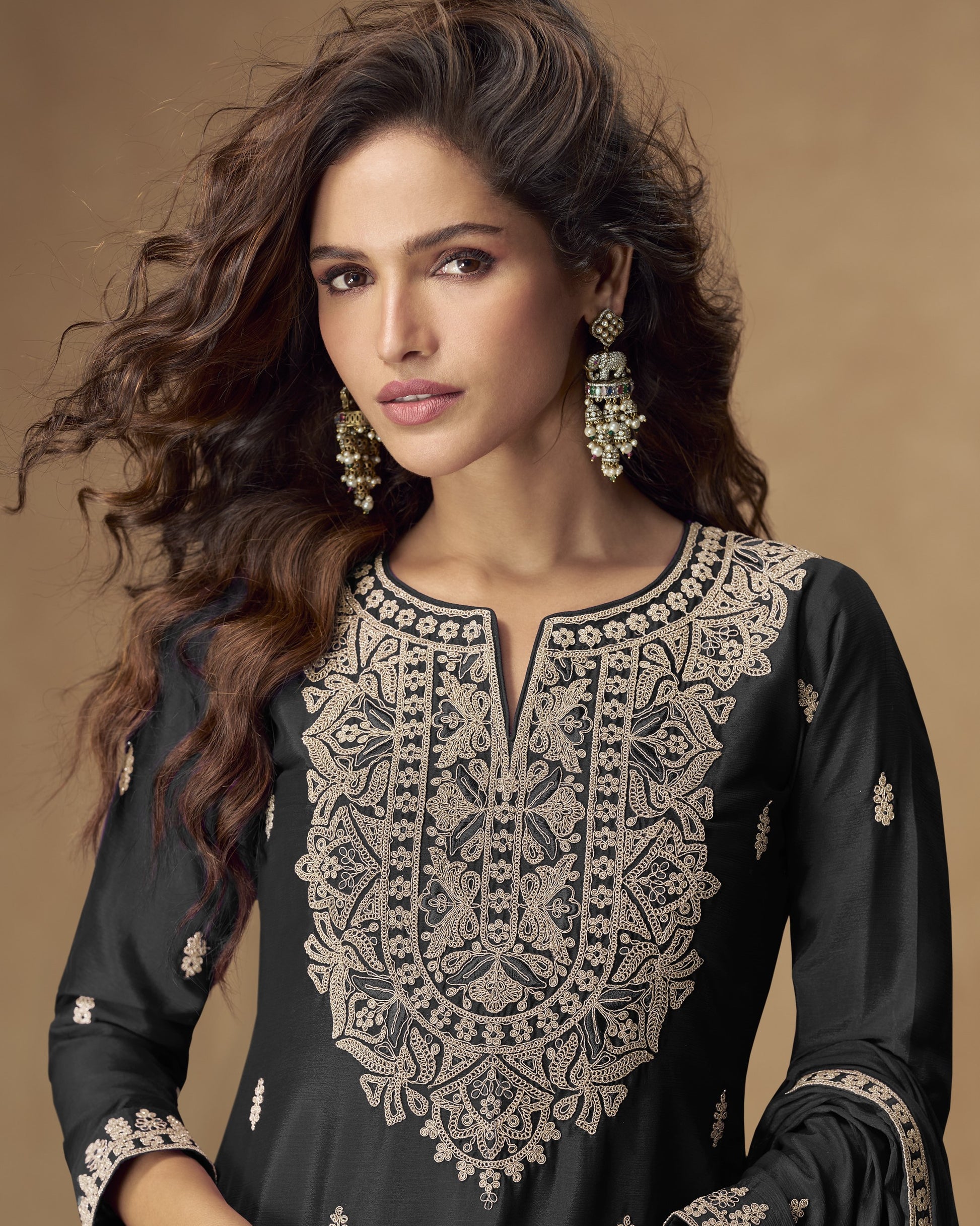 Woman wearing an embroidered black outfit with gold details on a brown background