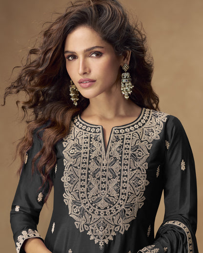 Woman wearing an embroidered black outfit with gold details on a brown background