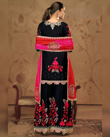 Woman wearing a black and red embroidered traditional outfit with a matching shawl.