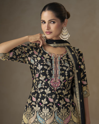 Woman wearing a black embroidered traditional outfit with gold details on a brown background
