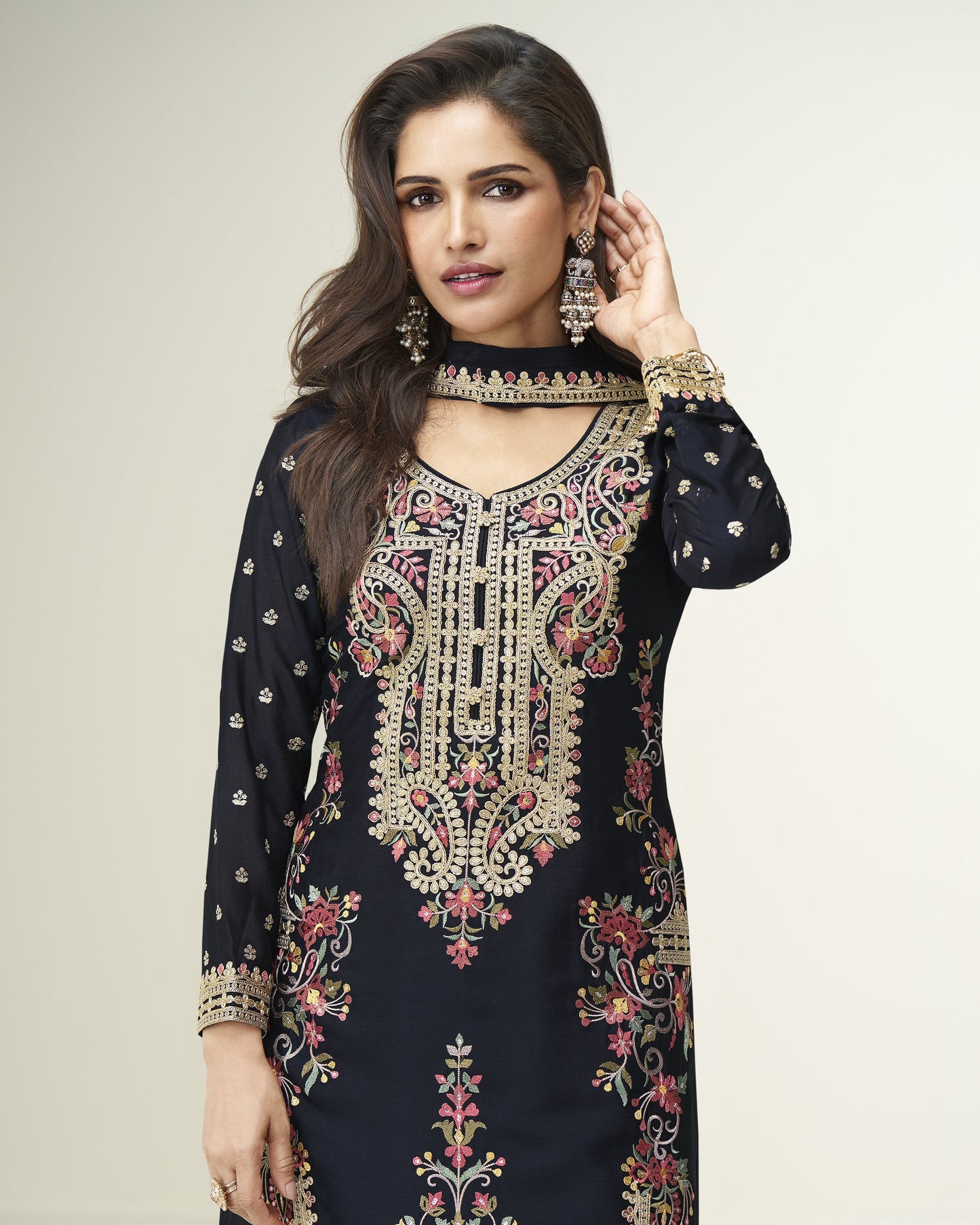 Woman wearing a black embroidered traditional outfit with gold detailing on a plain background