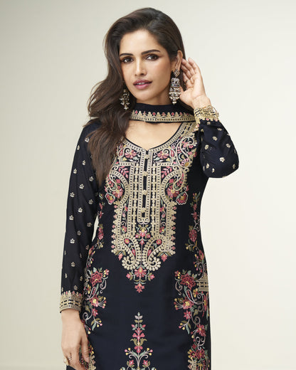 Woman wearing a black embroidered traditional outfit with gold detailing on a plain background