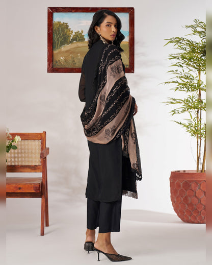Woman wearing a black outfit with a patterned shawl in a minimalistic room.