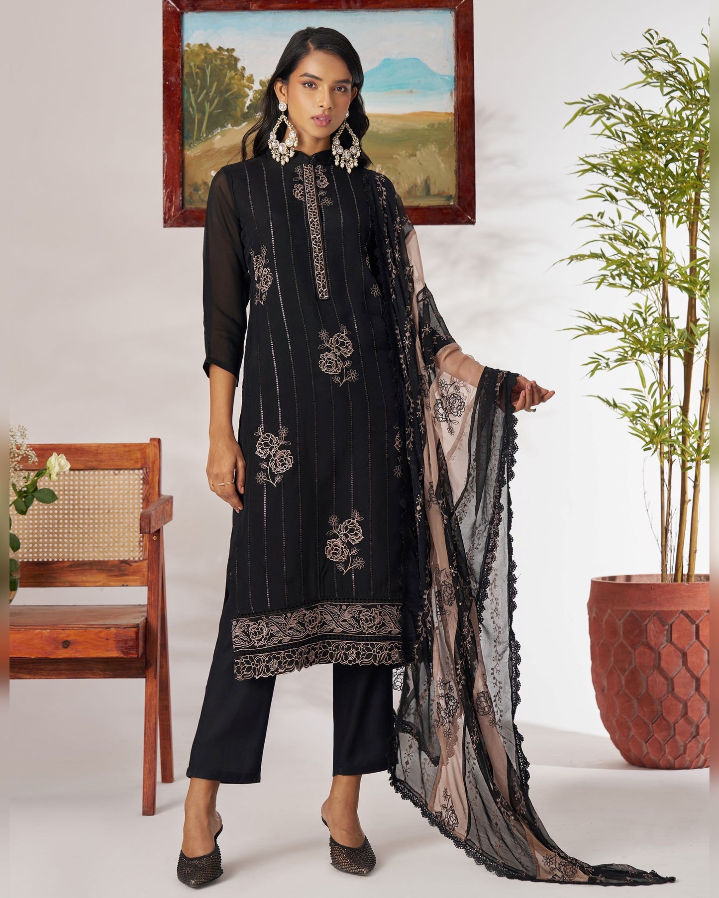 Woman in a black embroidered outfit standing indoors with decor elements.